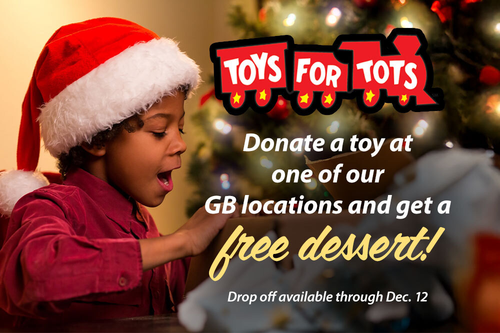 child in Santa hat looking into a box and smiling with wonder, with Christmas tree in background